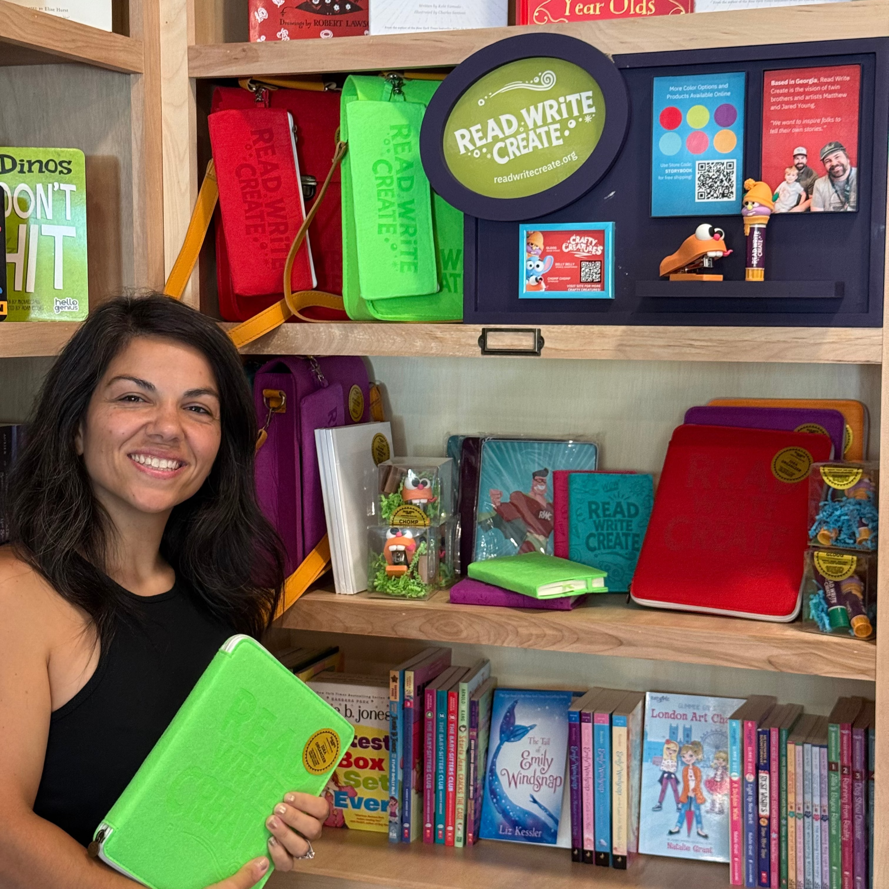 Woman holding a green book in front of a bookshelf filled with educational books and materials.