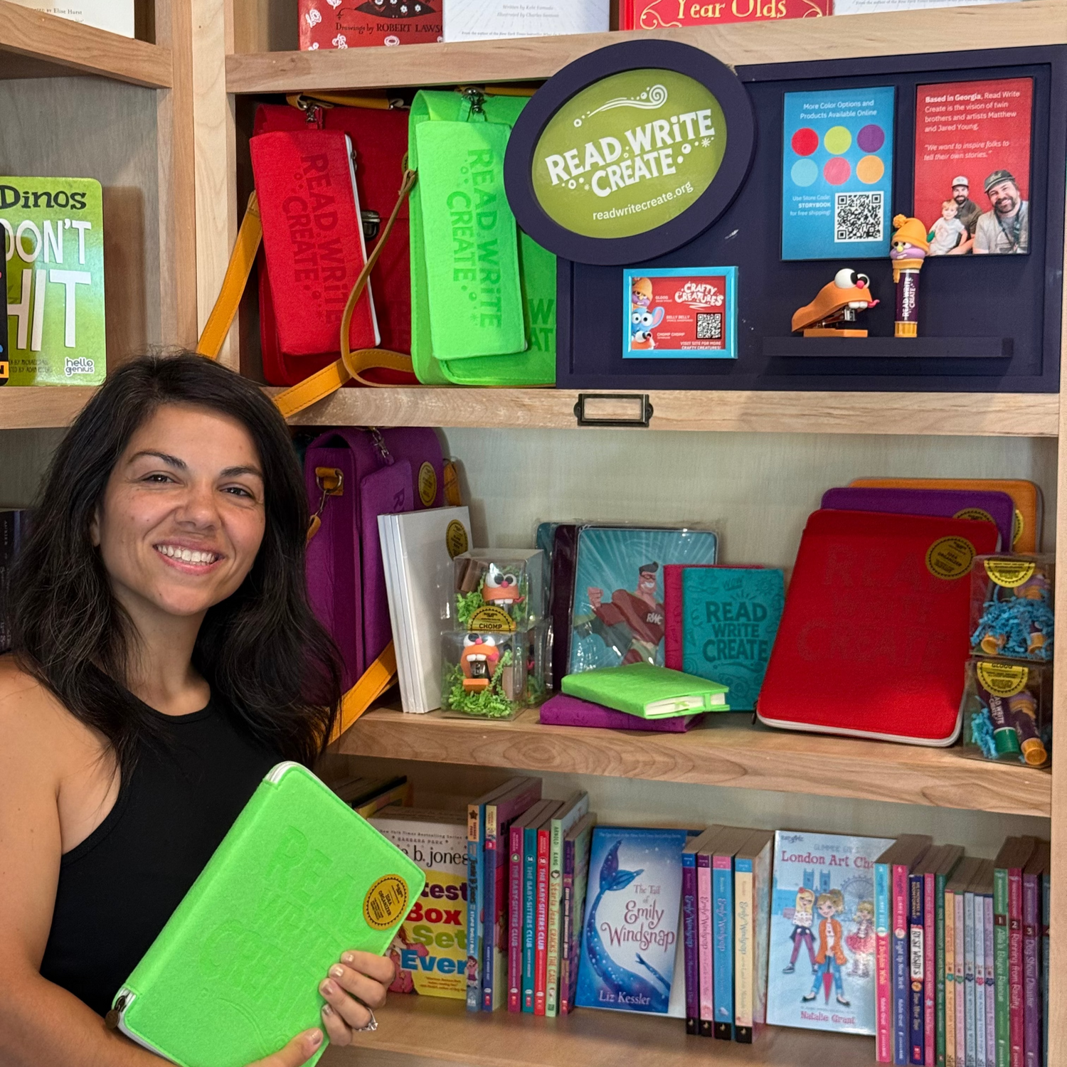Woman holding a green book in front of a bookshelf filled with educational books and materials.